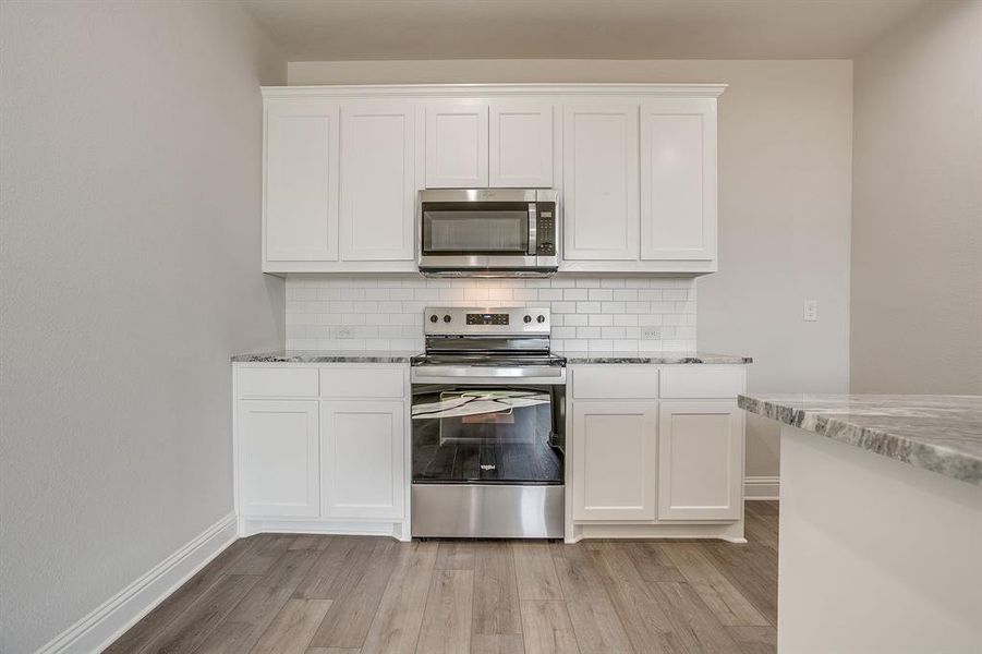 Kitchen featuring stainless steel appliances, light stone countertops, white cabinets, light wood finished floors, and tasteful backsplash