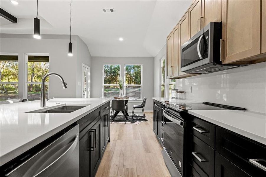 Kitchen featuring light brown cabinetry, a healthy amount of sunlight, lofted ceiling, and appliances with stainless steel finishes