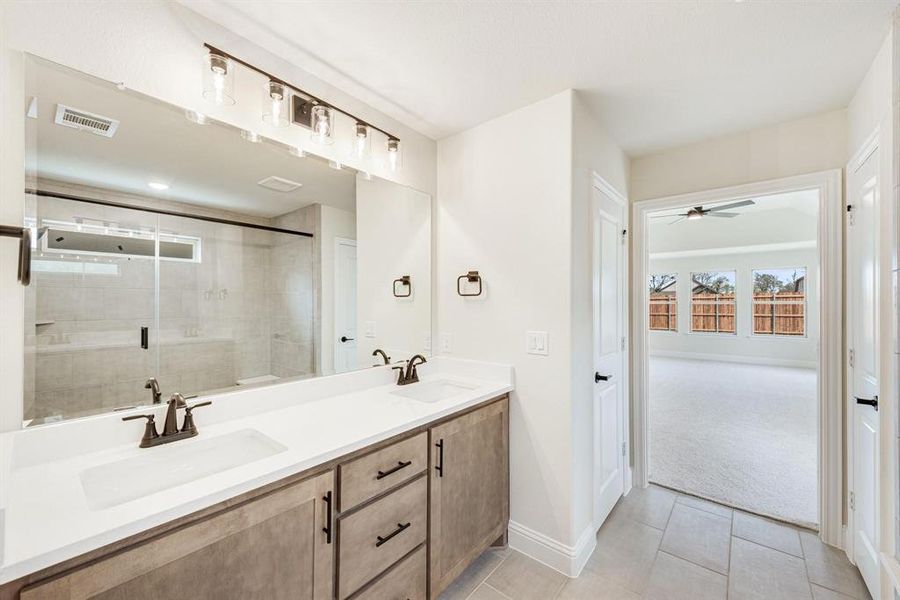 Bathroom featuring a stall shower, double vanity, light tile patterned flooring, and ceiling fan