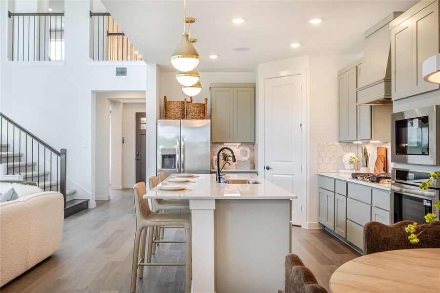 This photo showcases a modern kitchen with sleek cabinetry, a central island with seating, and stainless steel appliances. The space is bright and airy, featuring pendant lighting and an open layout that seamlessly connects to a staircase, adding a stylish touch to the home. This photo showcases a modern kitchen with sleek cabinetry, a central island with seating, and stainless steel appliances. The space is bright and airy, featuring pendant lighting and an open layout that seamlessly connects to a staircase, adding a stylish touch to the home.