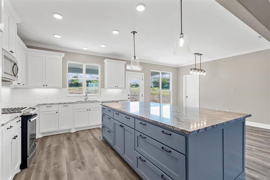 Kitchen featuring decorative light fixtures, white cabinetry, appliances with stainless steel finishes, and a center island