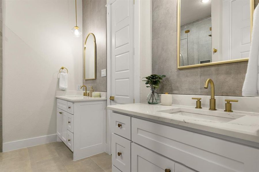 Bathroom featuring baseboards, two vanities, a sink, and tiled shower