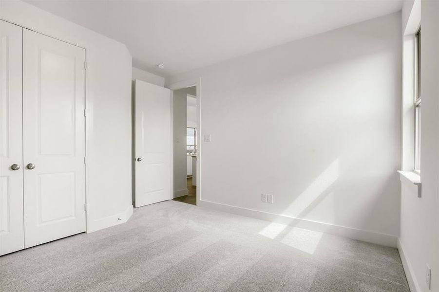 Neutral-toned room featuring a window with natural light, light gray carpeting, and white baseboards