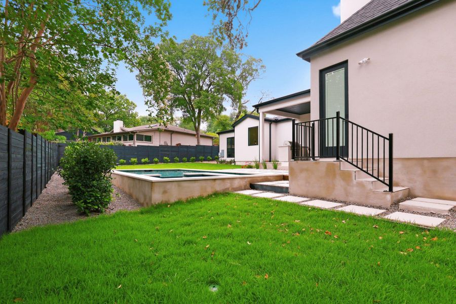 Rear exterior featuring a built-in spa, concrete stepping stones, a black privacy fence, and a covered patio area