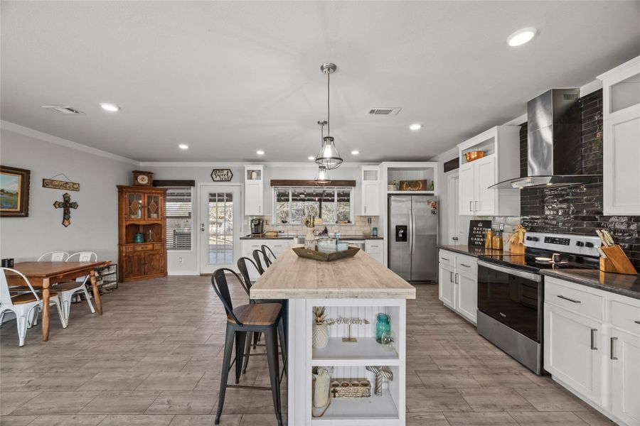 Kitchen with open shelves, a breakfast bar area, stainless steel appliances, glass insert cabinets, and ornamental molding
