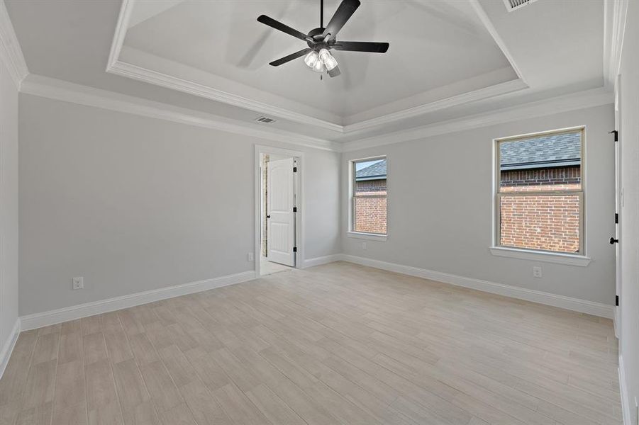 Empty room with a tray ceiling, crown molding, light wood-type flooring, and a ceiling fan Empty room with a tray ceiling, crown molding, light wood-type flooring, and a ceiling fan