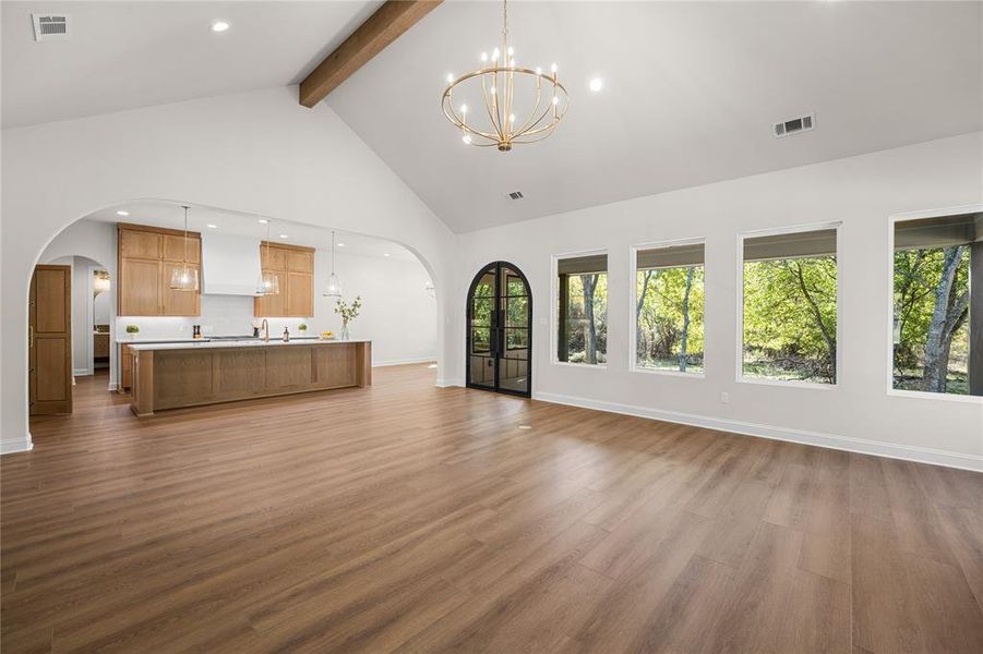 Unfurnished living room with beamed ceiling, high vaulted ceiling, arched walkways, dark wood-style floors, and a chandelier