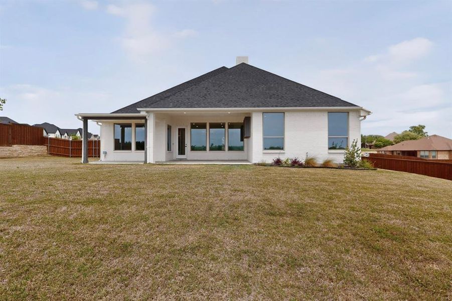 Spacious backyard featuring a covered patio, multiple large windows, white brick exterior, dark shingle roof, and wooden privacy fencing Spacious backyard featuring a covered patio, multiple large windows, white brick exterior, dark shingle roof, and wooden privacy fencing