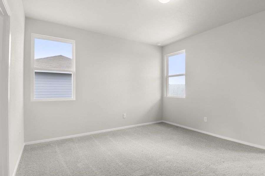Image of primary bedroom with light grey walls and carpet with two windows