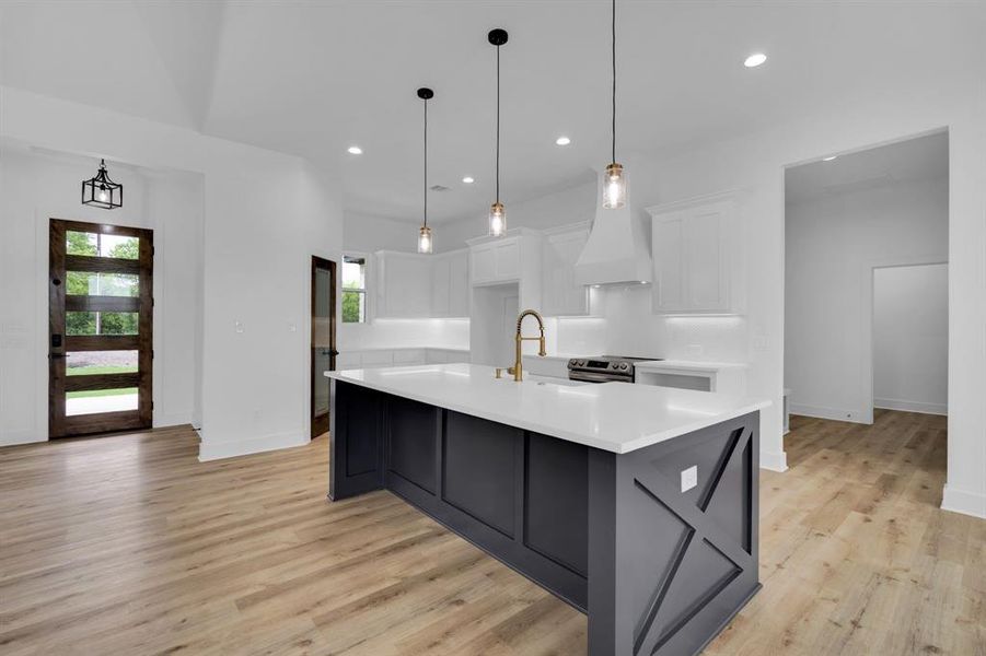 Kitchen featuring hanging light fixtures, white cabinets, custom exhaust hood, a center island with sink, and light hardwood / wood-style floors