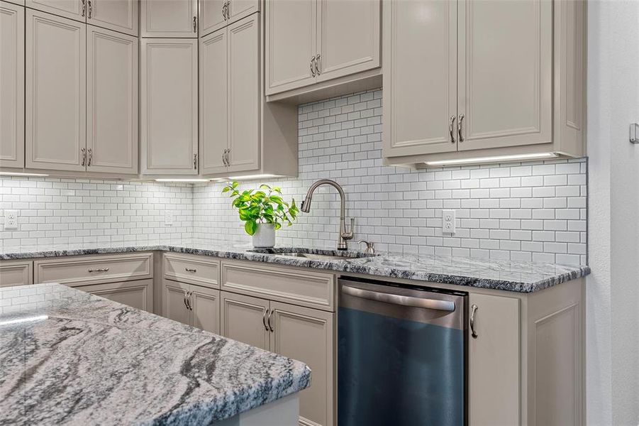 Kitchen featuring dishwasher, backsplash, and light stone countertops Kitchen featuring dishwasher, backsplash, and light stone countertops