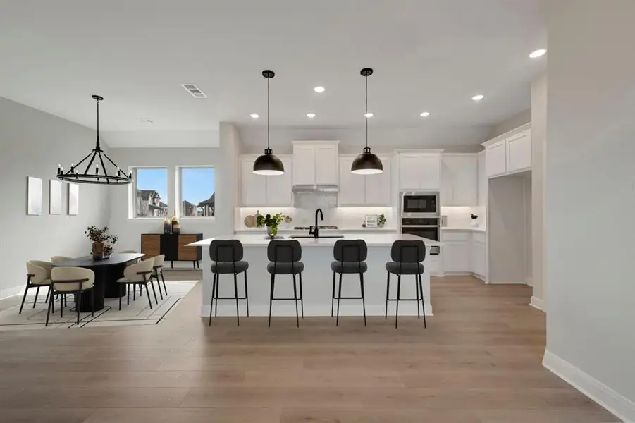 Kitchen with a breakfast bar area, white cabinetry, an island with sink, built in microwave, and light wood-style flooring