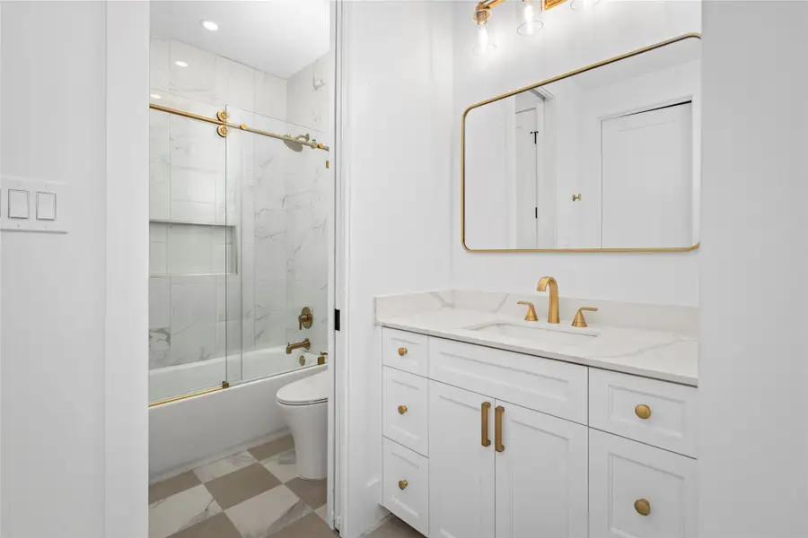 Stylish Jack-and-Jill bath featuring quartz countertops, custom cabinetry, brushed-gold fixtures, and a tub/shower combination with a floor-to-ceiling marble porcelain tile surround and a built-in niche. Stylish Jack-and-Jill bath featuring quartz countertops, custom cabinetry, brushed-gold fixtures, and a tub/shower combination with a floor-to-ceiling marble porcelain tile surround and a built-in niche.