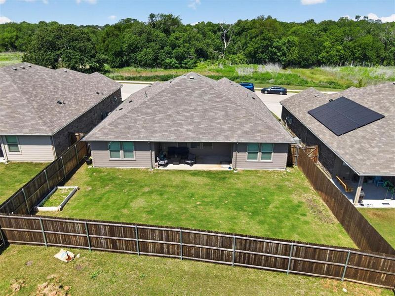 Expansive fenced backyard featuring a covered patio, manicured lawn, and a raised garden bed
