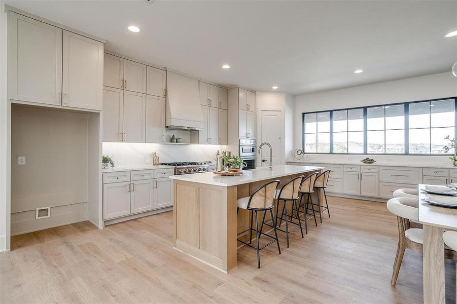 Kitchen with premium range hood, light wood-type flooring, a kitchen breakfast bar, light countertops, and tasteful backsplash