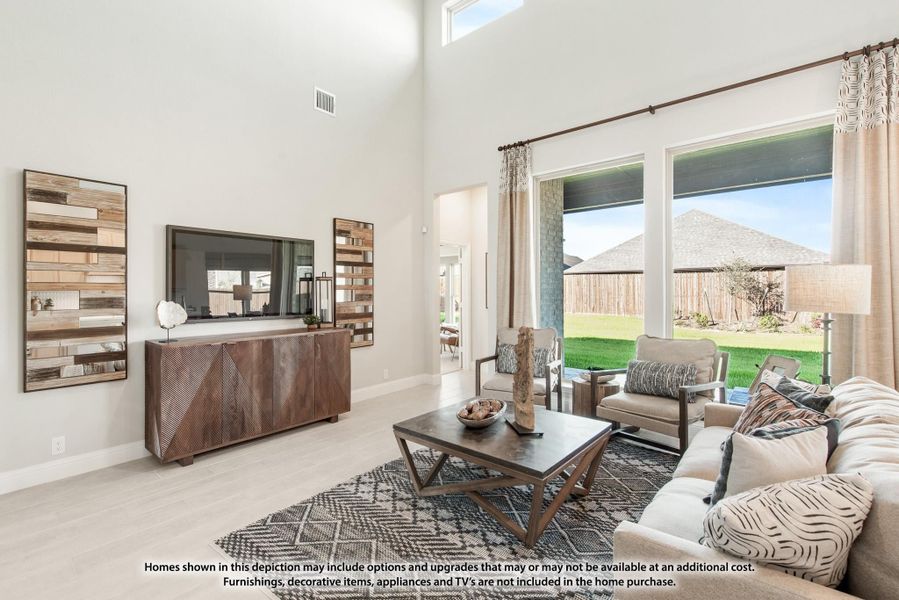 Living room with two-story ceiling, large windows overlooking backyard, and wood media console with wall-mounted TV