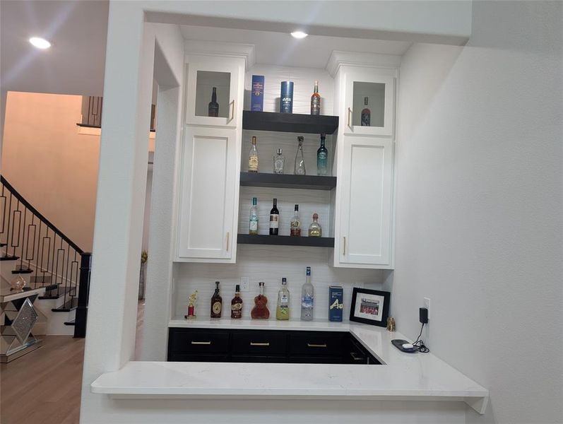 Indoor dry bar with tasteful backsplash, wood finished floors, and stairs