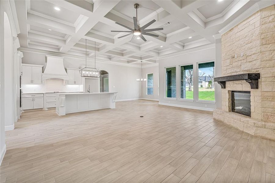Unfurnished living room with a chandelier, ceiling fan, light wood-style flooring, beamed ceiling, and coffered ceiling