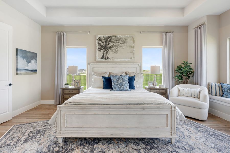 Master bedroom with white wood bed frame, hardwood floors, tray ceiling, and two windows with backyard views