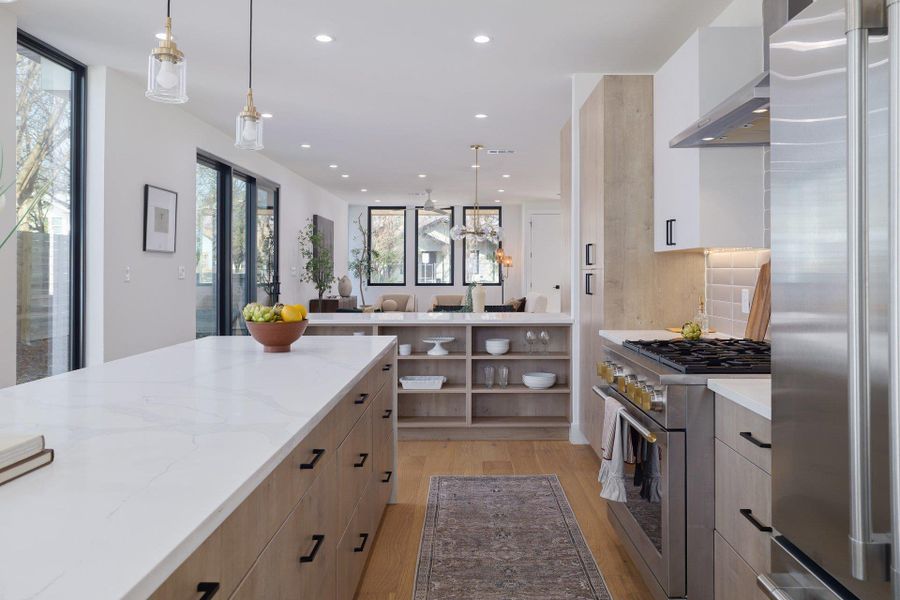Kitchen featuring dual tone cabinets, decorative light fixtures, premium appliances, open shelves, and light wood-style floors