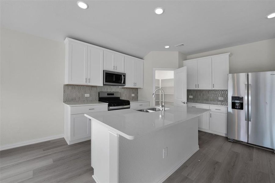 Kitchen featuring appliances with stainless steel finishes, white cabinets, a center island with sink, light wood finished floors, and recessed lighting Kitchen featuring appliances with stainless steel finishes, white cabinets, a center island with sink, light wood finished floors, and recessed lighting