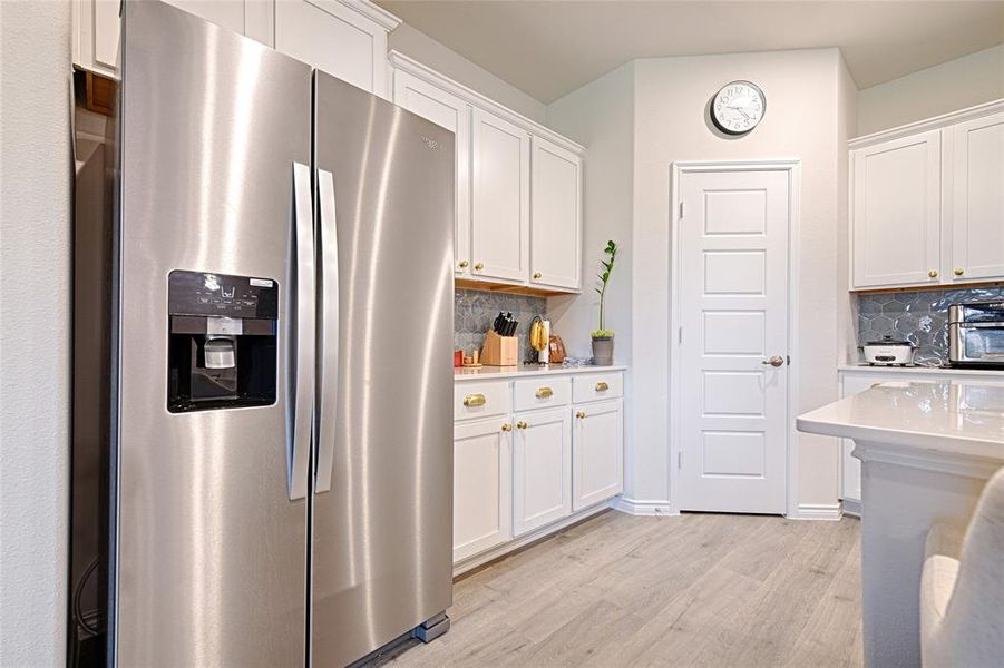 Kitchen with white cabinetry, decorative backsplash, stainless steel fridge with ice dispenser, and light wood-type flooring