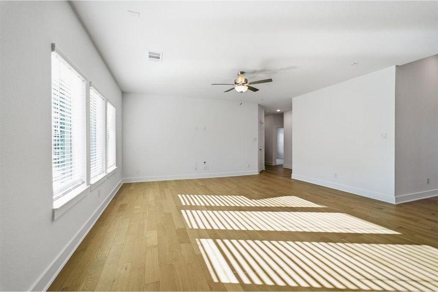 Spacious interior featuring light wood-finish flooring, multiple windows with blinds, a ceiling fan with integrated lighting, and neutral wall tones Spacious interior featuring light wood-finish flooring, multiple windows with blinds, a ceiling fan with integrated lighting, and neutral wall tones