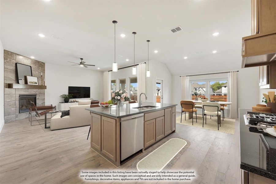 Open-concept kitchen with large island, pendant lights, and views into living and dining areas with stone fireplace