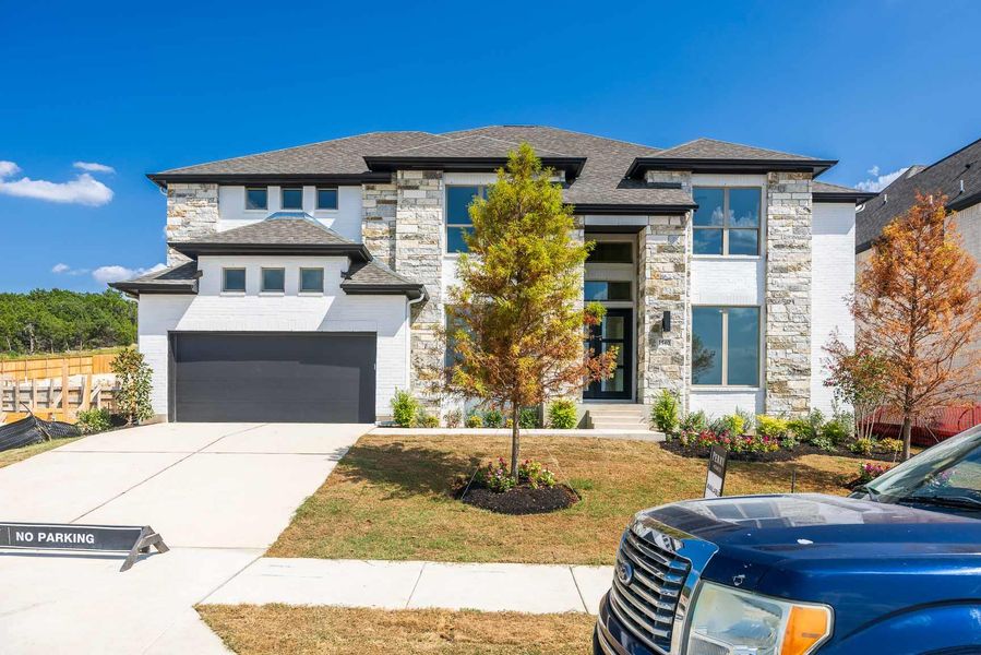 Prairie-style house with stone siding, concrete driveway, an attached garage, a shingled roof, and a front lawn