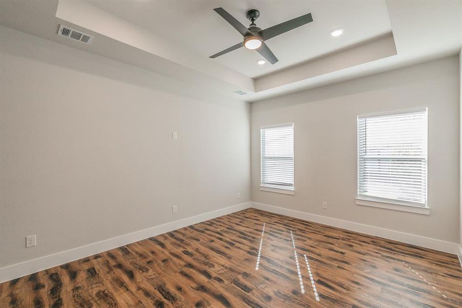 Unfurnished room featuring a raised ceiling, ceiling fan, and dark wood-type flooring