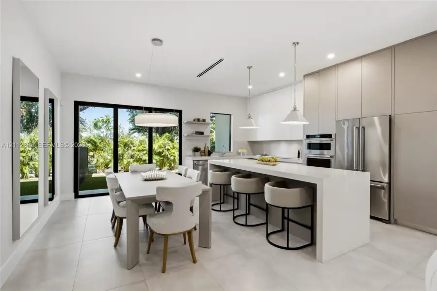 Kitchen featuring a waterfall-edge island with solid-surface countertops, floor-to-ceiling flat-panel cabinetry, stainless steel built-in appliances, pendant lighting, and large-format porcelain tile flooring