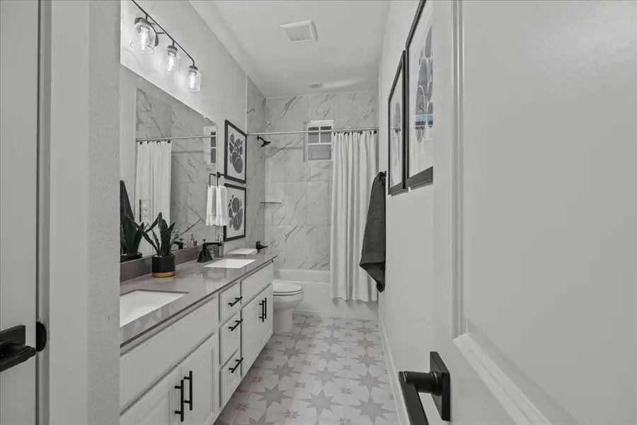 Bathroom featuring double vanity, shower / bath combo, toilet, and tile patterned floors Bathroom featuring double vanity, shower / bath combo, toilet, and tile patterned floors