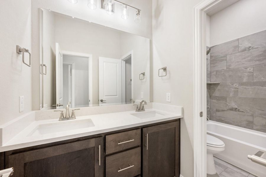 Bathroom with double sink vanity, dark wood cabinets, and tiled bathtub surround