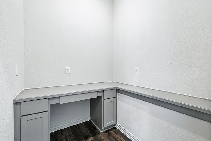 Unfurnished office with dark wood-type flooring, built in desk, and a textured wall Unfurnished office with dark wood-type flooring, built in desk, and a textured wall