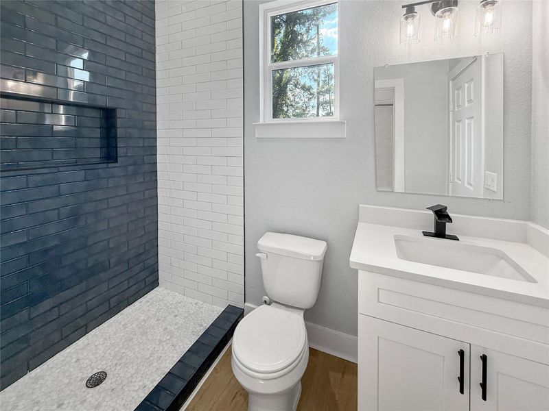 A  beautifully upscale bathroom featuring a modern subway tile shower with black fixtures, and bright natural light streaming through the window for a fresh and inviting ambiance.