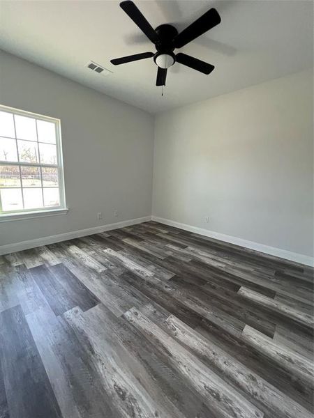 Spare room featuring dark wood-type flooring, baseboards, visible vents, and ceiling fan