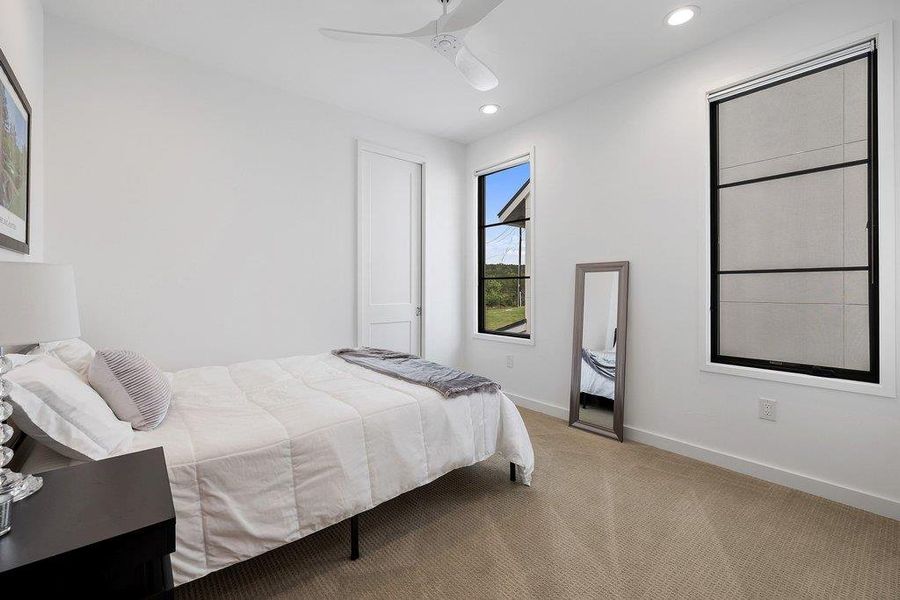 Carpeted room featuring two prominent windows with black frames, a ceiling fan, and recessed lighting