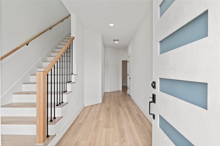 Step into a bright, airy foyer defined by clean lines, warm wood-toned flooring, and a seamless modern stair rail.
