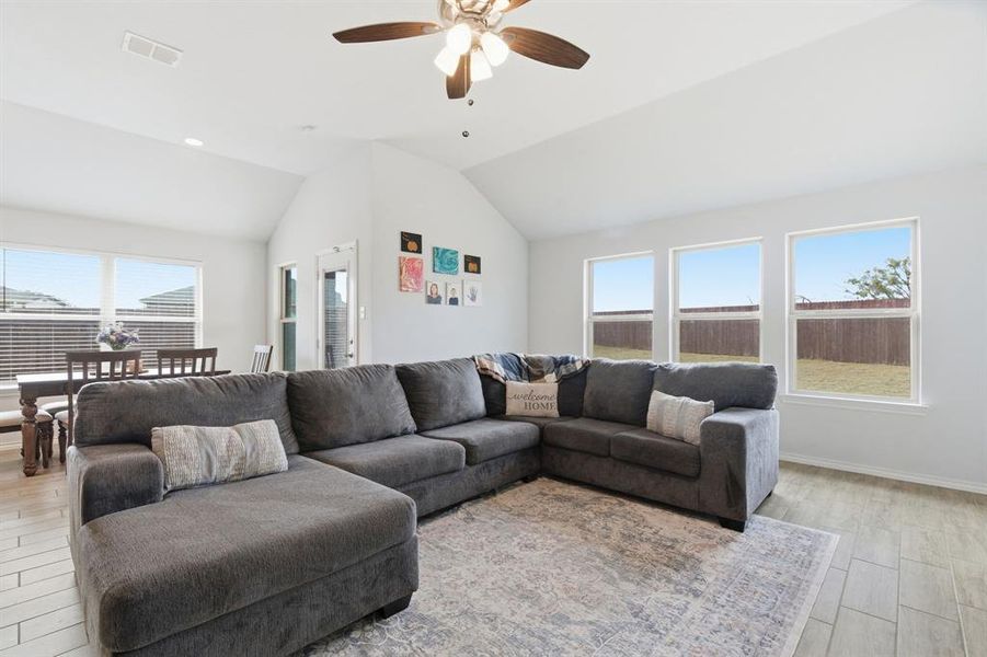 Living room featuring light wood-style floors, healthy amount of natural light, vaulted ceiling, a ceiling fan, and recessed lighting
