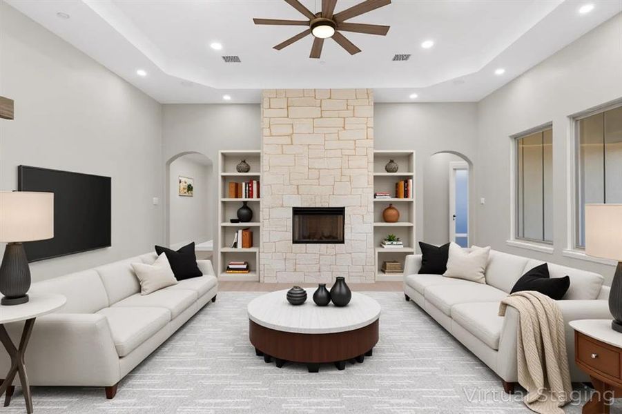 Living area with arched walkways, a stone fireplace, a ceiling fan, a raised ceiling, and recessed lighting