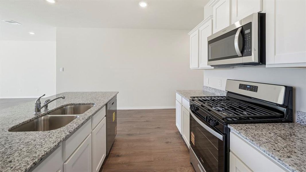 Kitchen featuring appliances with stainless steel finishes, white cabinets, dark wood-type flooring, light stone countertops, and recessed lighting