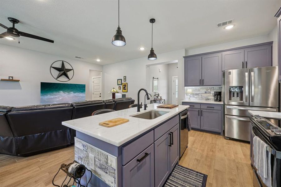 Kitchen with open floor plan, stainless steel appliances, pendant lighting, gray cabinetry, and light wood-type flooring Kitchen with open floor plan, stainless steel appliances, pendant lighting, gray cabinetry, and light wood-type flooring