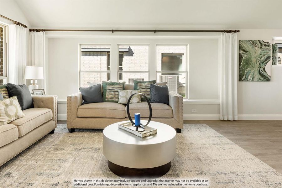 Living room with beige sofas, round coffee table, hardwood floors, and large windows with white curtains