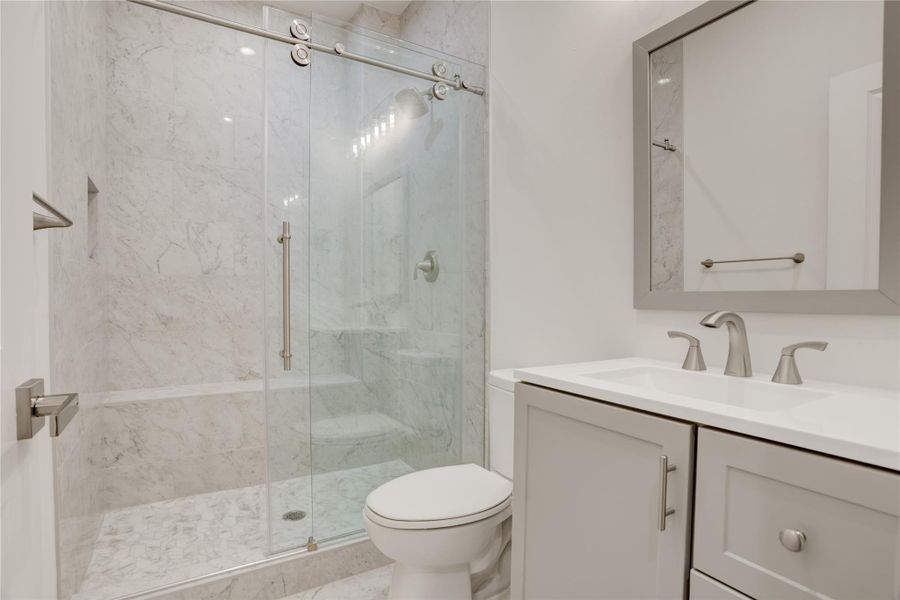 Contemporary full bath off third bedroom with frameless glass walk in shower and sleek tile detail.