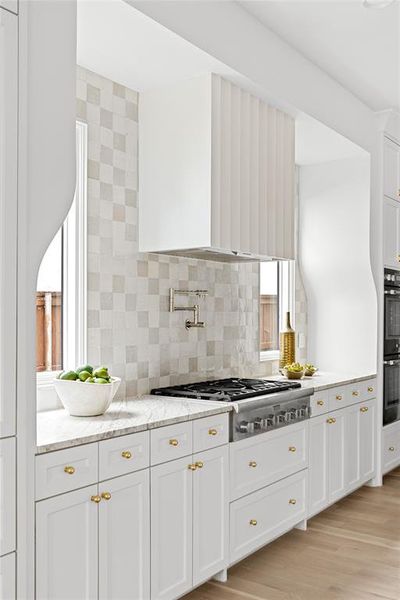 Kitchen featuring white cabinets, light stone countertops, stainless steel gas stovetop, backsplash, and light wood-style floors