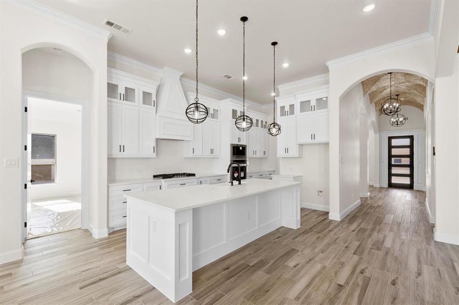 Kitchen with decorative light fixtures, white cabinetry, appliances with stainless steel finishes, and a center island with sink