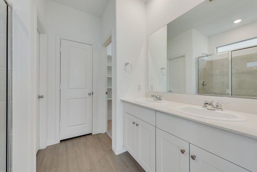 Bathroom featuring a stall shower, double vanity, wood finished floors, and a walk in closet Bathroom featuring a stall shower, double vanity, wood finished floors, and a walk in closet