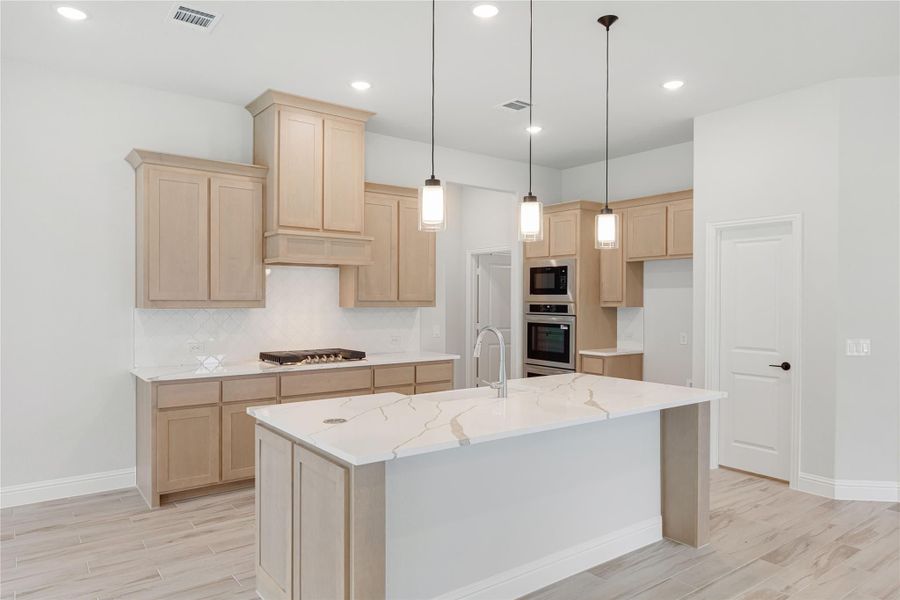 Kitchen with light wood cabinets, quartz island, pendant lights, and stainless steel appliances on light wood floors Kitchen with light wood cabinets, quartz island, pendant lights, and stainless steel appliances on light wood floors