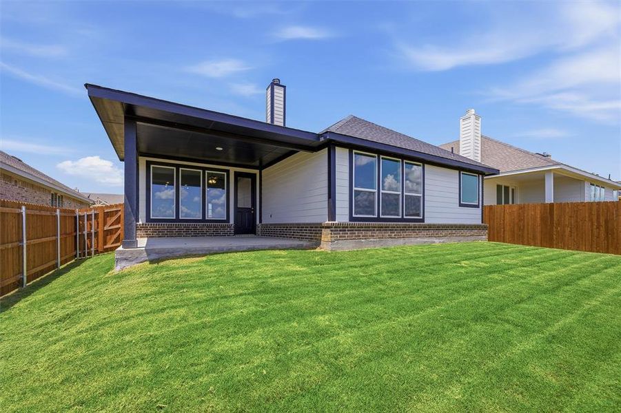 Rear exterior featuring a covered patio, expansive lawn, white siding, dark trim windows, and a brick foundation Rear exterior featuring a covered patio, expansive lawn, white siding, dark trim windows, and a brick foundation