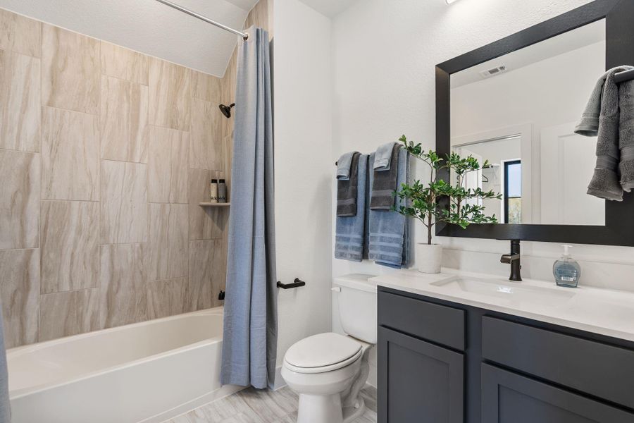 A well-appointed secondary bathroom featuring a tub/shower combination accented by tile work that extends seamlessly to the ceiling, creating a clean and sophisticated finish.